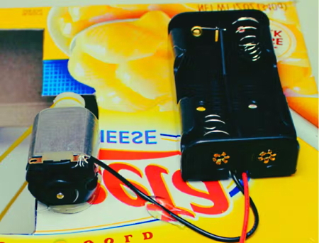 آرمیچر و نگهدارنده باتری روی یک سطح زرد با سیم سیاه به هم متصل شده‌اند.