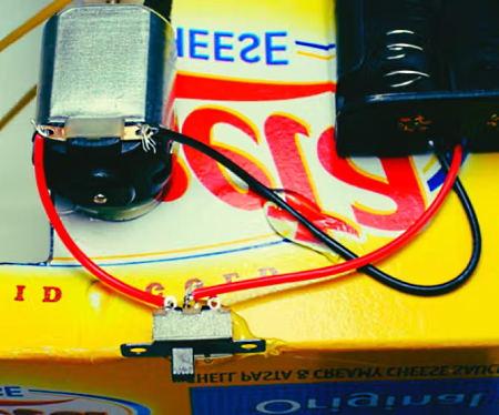آرمیچر و نگهدارنده باتری روی یک سطح زرد با سیم سیاه و قرمز به هم متصل شده‌اند.